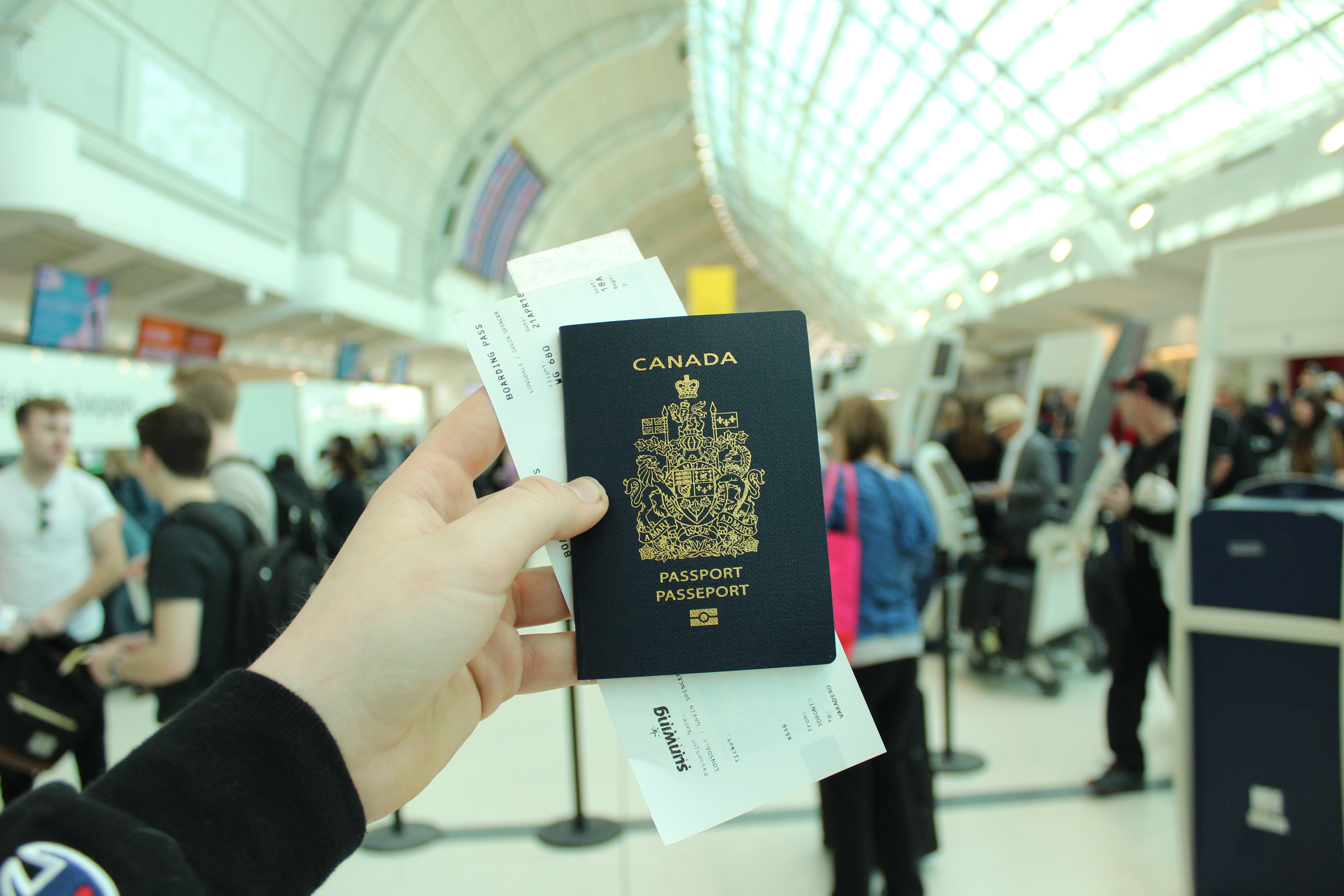 A hand holding a Canadian passport and boarding passes in an airport