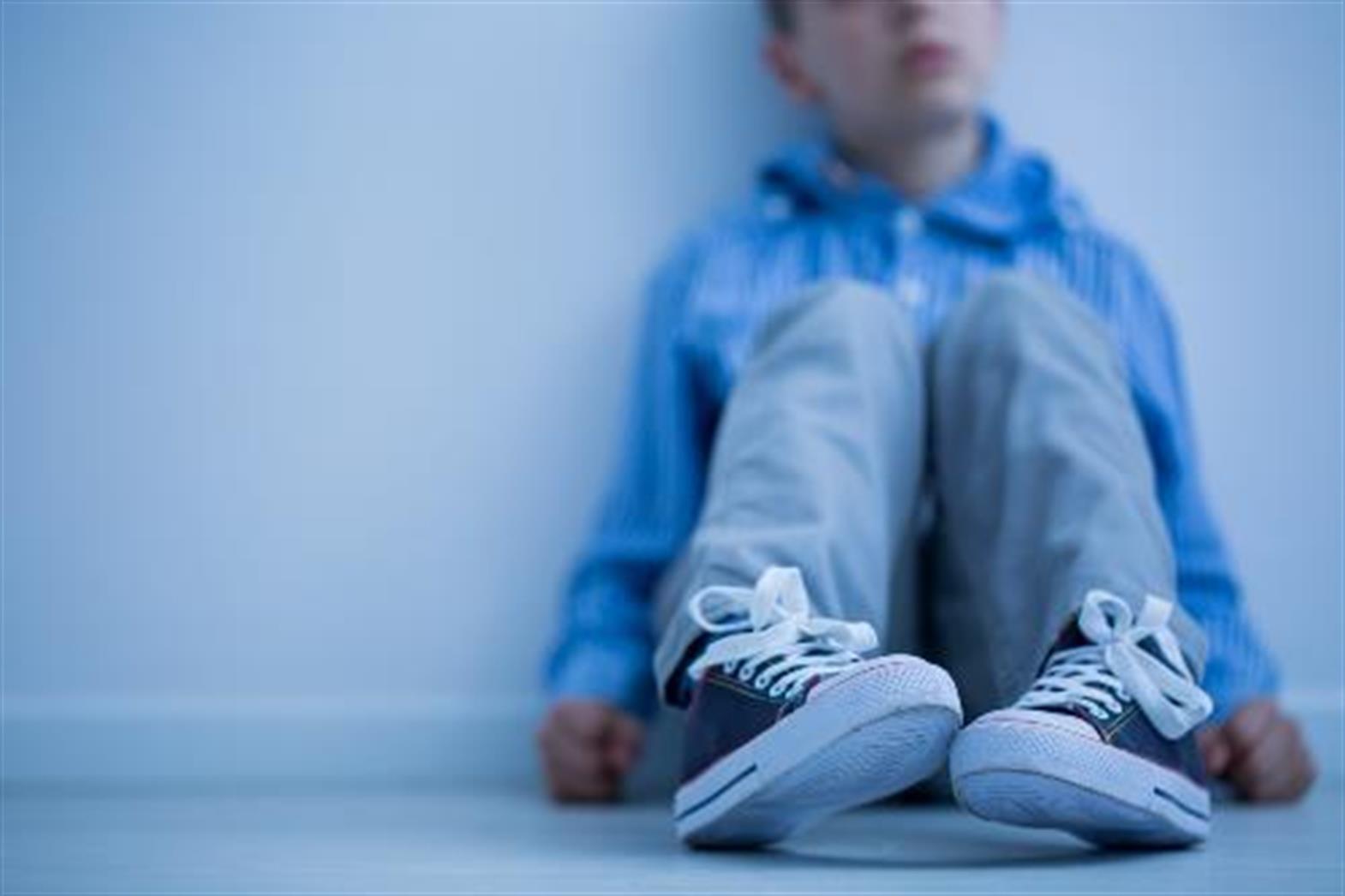 a boy about 9 years old sitting on the floor against a wall, thinking. 