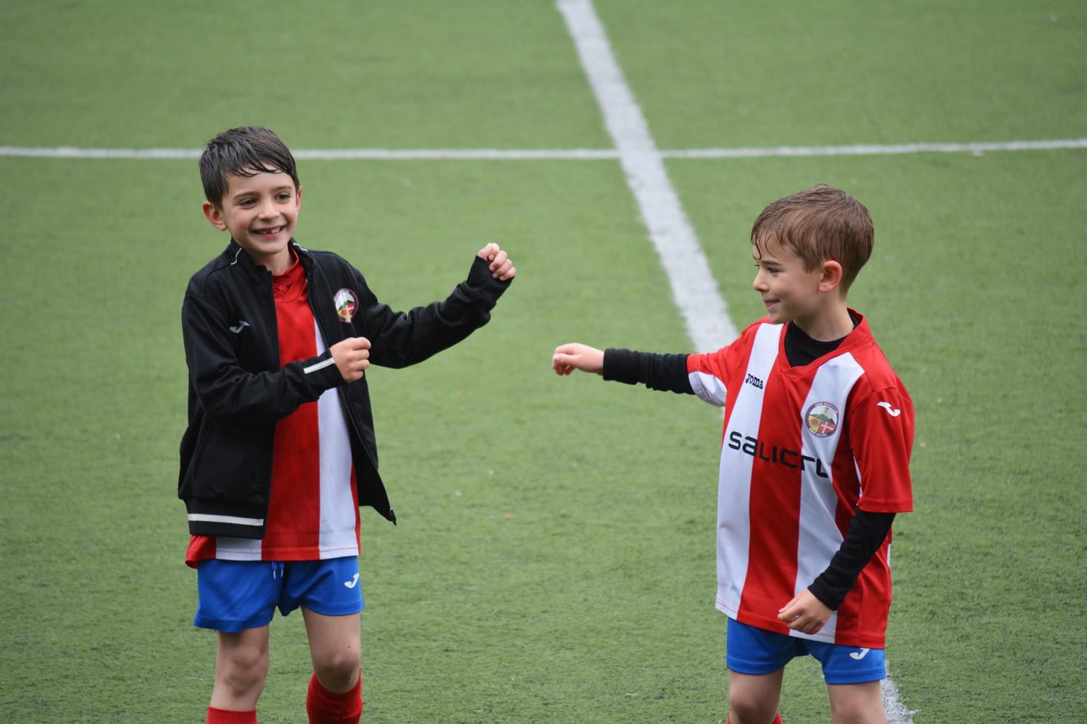 Two boys on a soccer field in socer uniforms smiling and laughing
