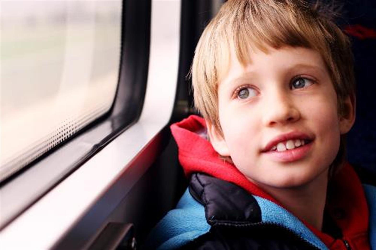 Boy about 9 years old looks out of a train window smiling