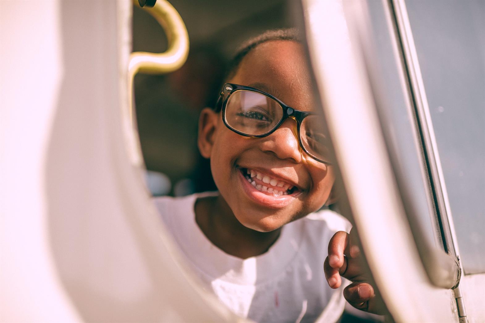 Child wearing glasses looking out a window and smiling