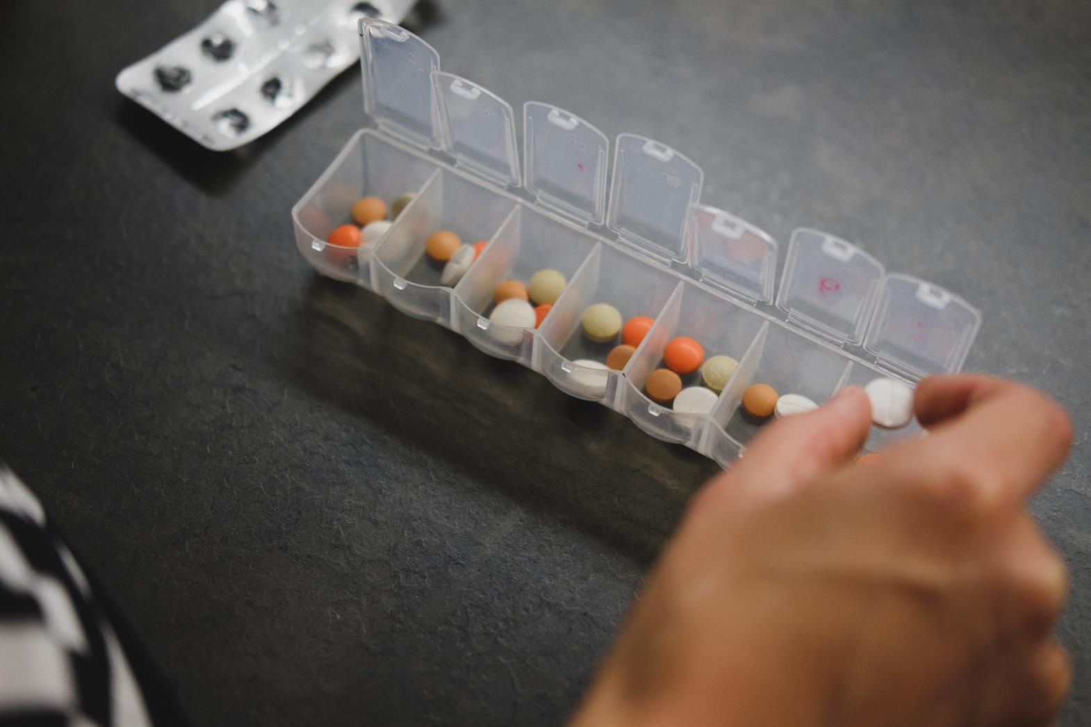 A weekly pill organizer with many pills in it. A hand is taking one of the pills out of the organizer