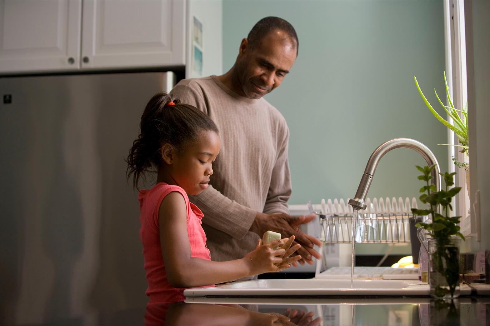 A father watching his daughter wash her hands by a kitchen sink