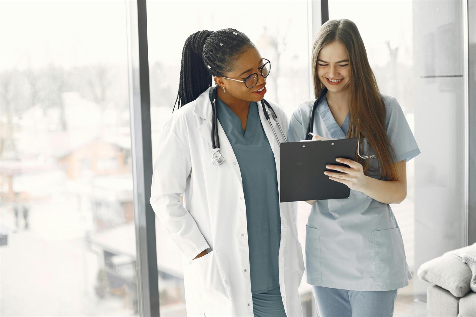 A doctor and a nurse talking in front of a window