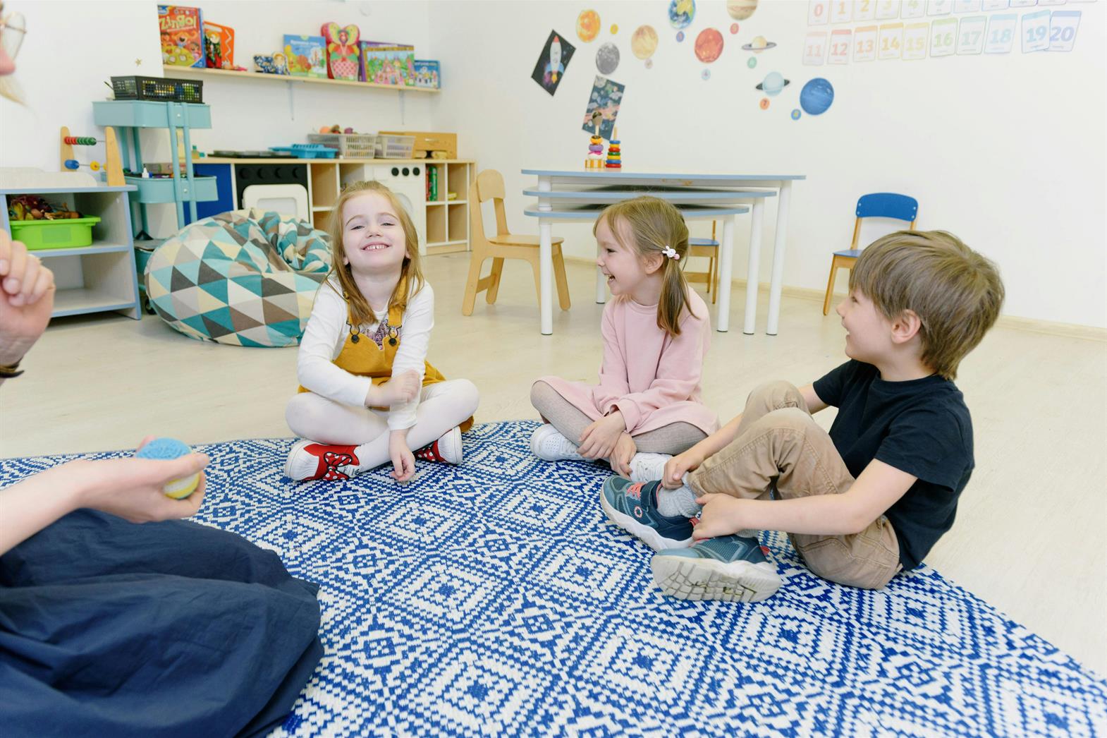 trois enfants assis sur un tapis dans une salle de classe