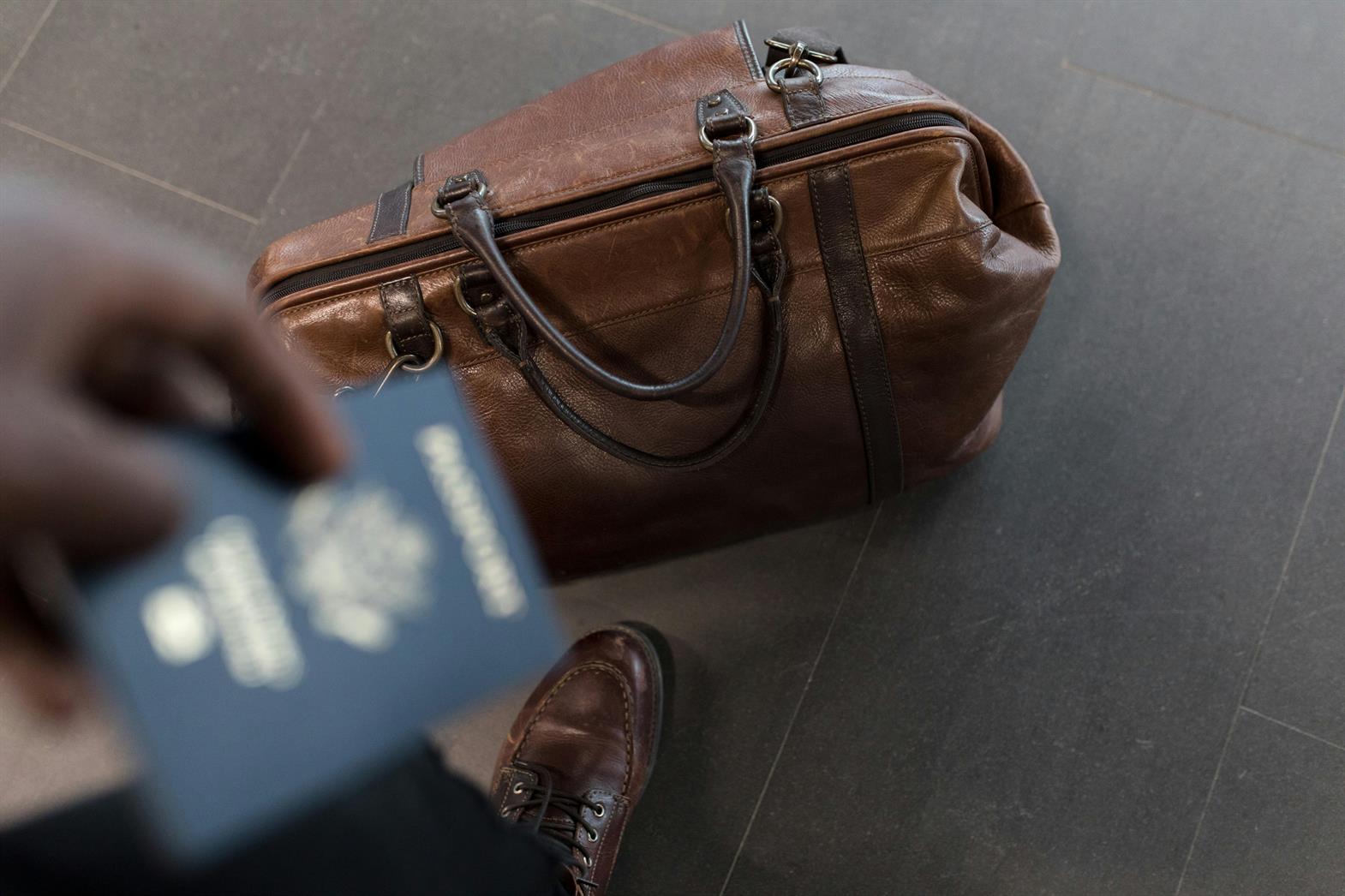 A traveler with a passport and a brown leather duffle bag