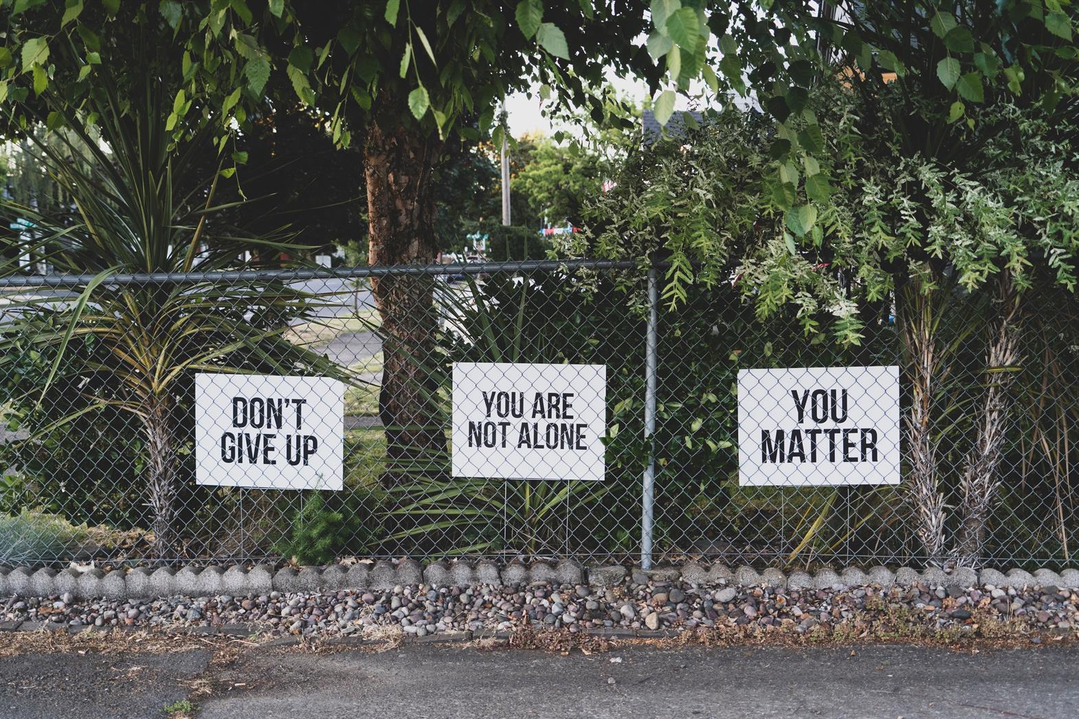 Signs on a fence that read: don't give up, you are not alone, you matter