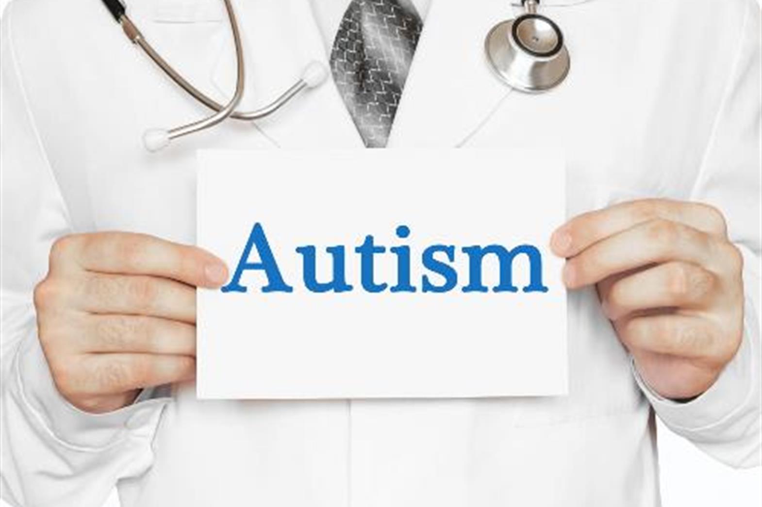 a person in a white lab coat wearing a stethoscope holding a sign that reads "autism"  