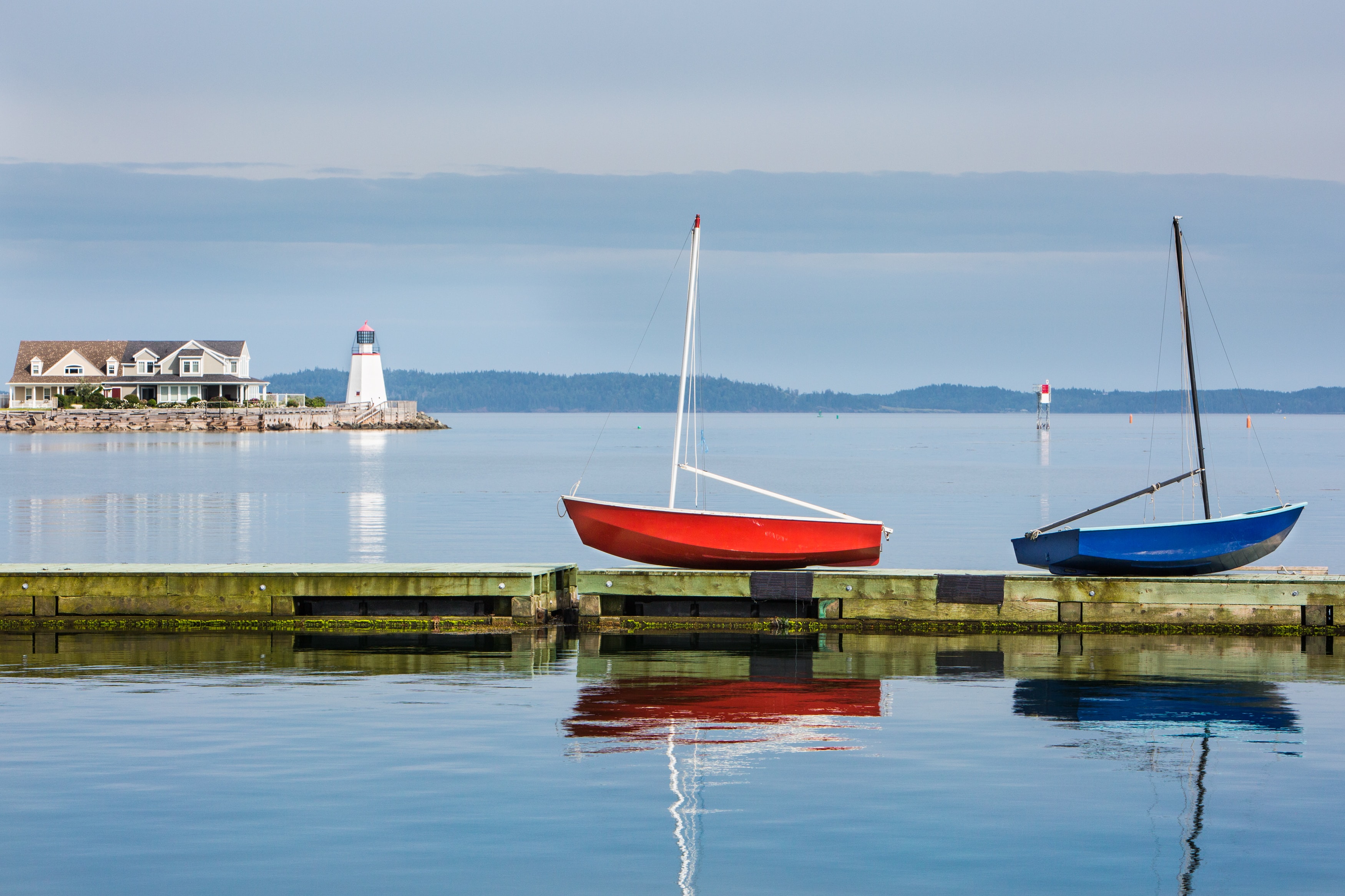 Two colourful boats on the water, A light house and some hills in the background