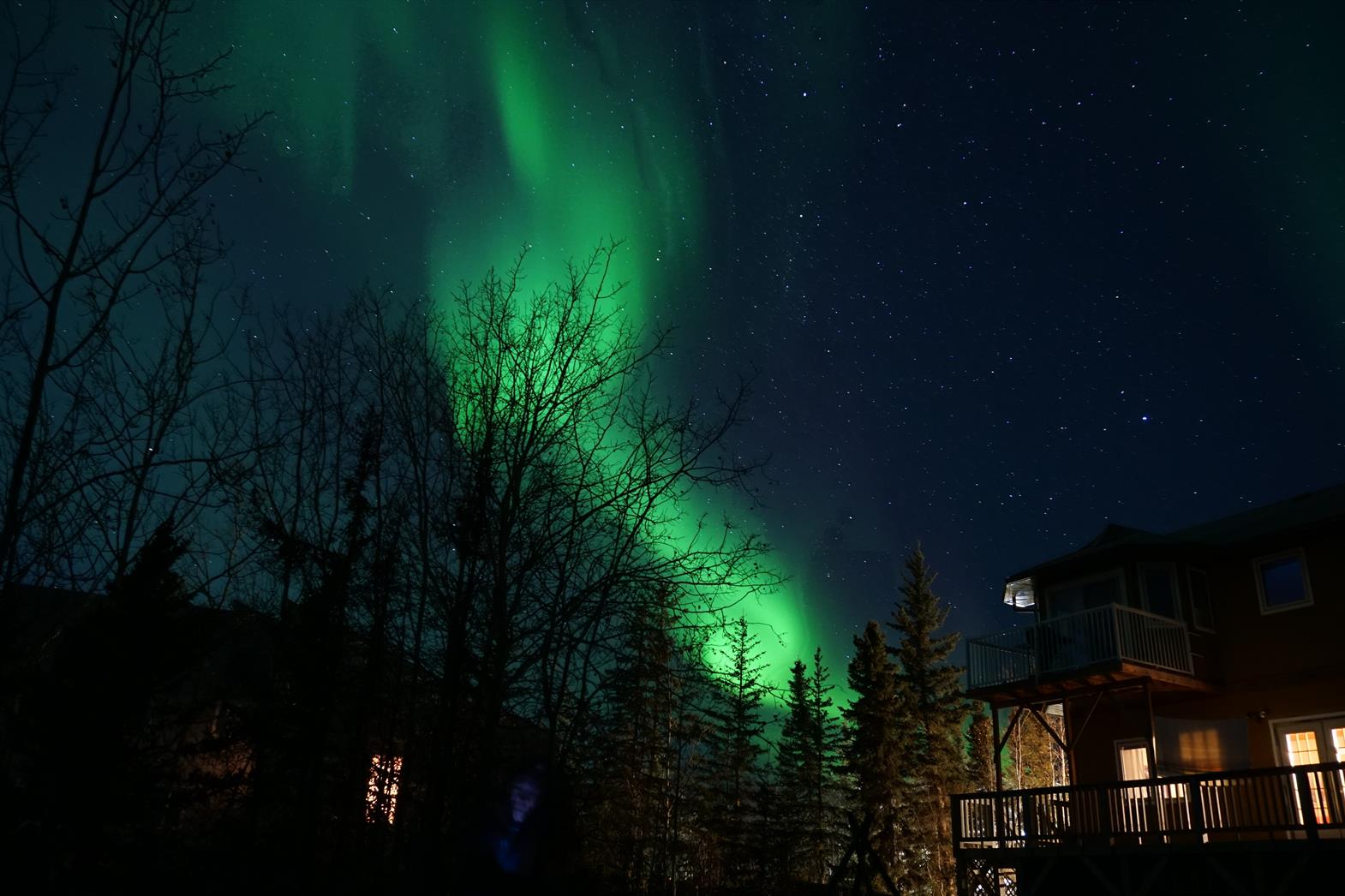 Norther lights in the night sky over a warmly lit house.
