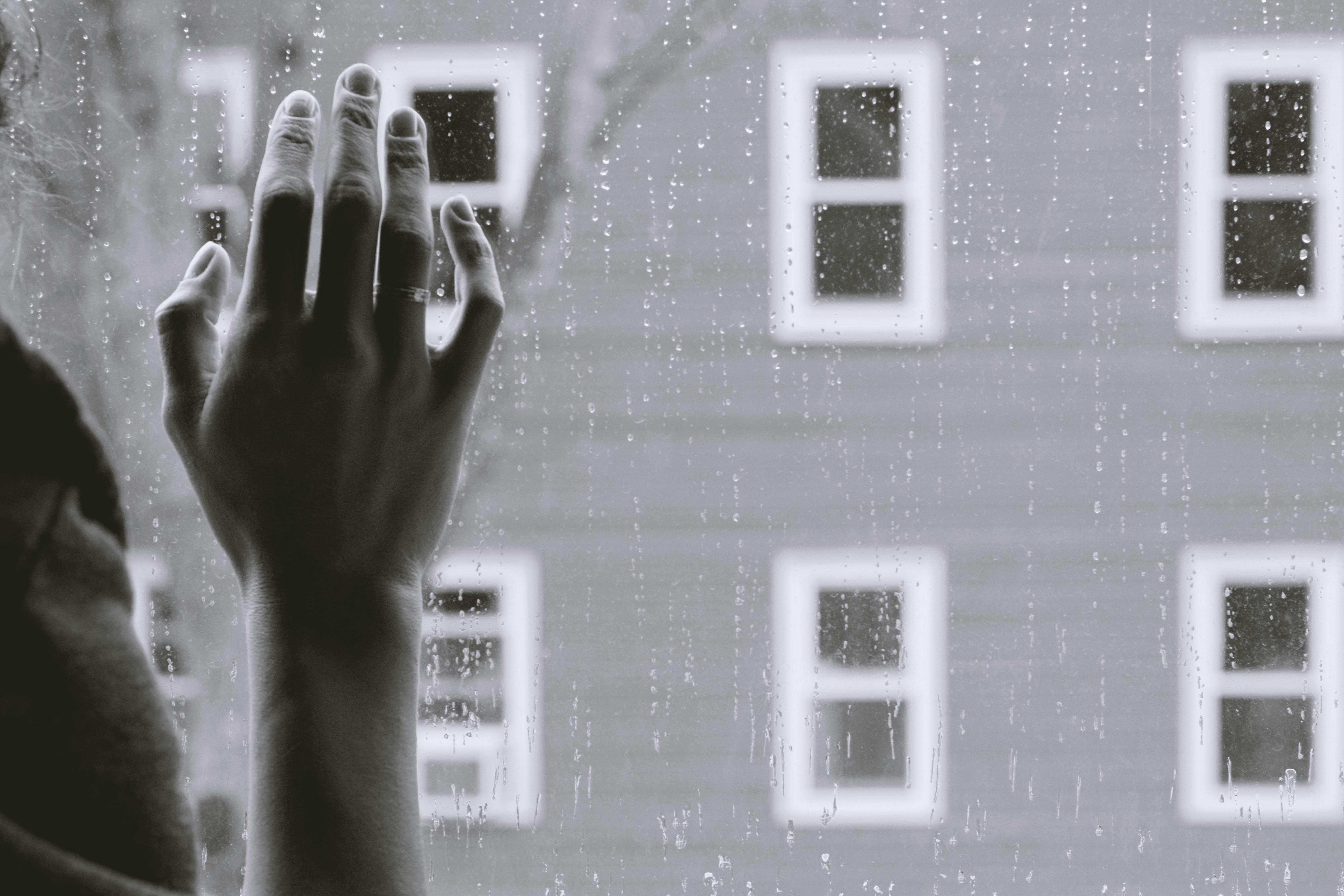 grayscale photo of a woman placing her right hand on a windowpane on a rainy day