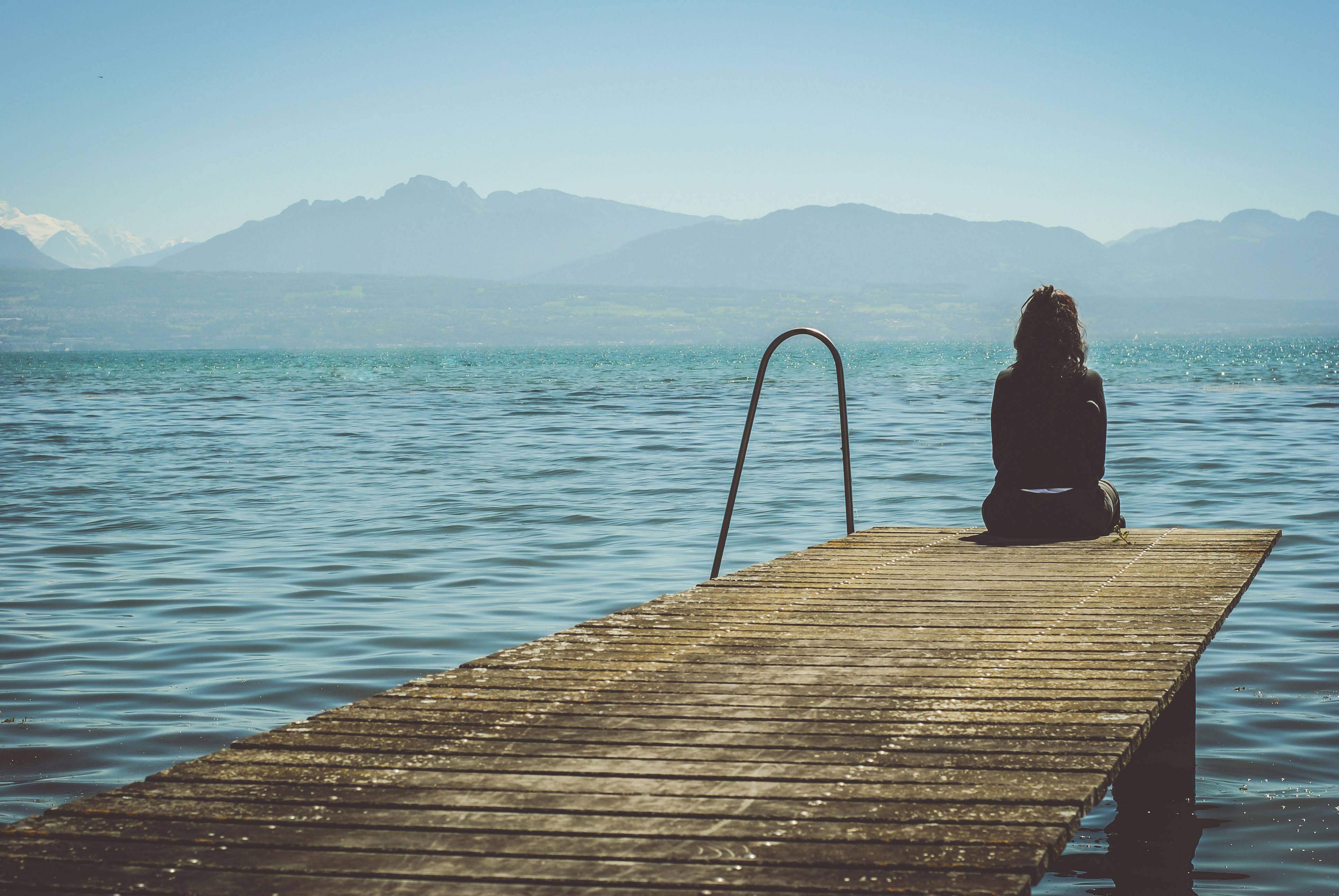 une femme assise à l'extrémité d'un quai pendant la journée regarde un lac.